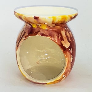May include: A ceramic oil burner with a round, open top and a wide, round opening on the side. The burner is decorated with a marbled pattern in shades of yellow, orange, and brown.