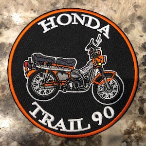 May include: A black and orange embroidered patch with the text "HONDA TRAIL 90" and a black and orange motorcycle illustration.