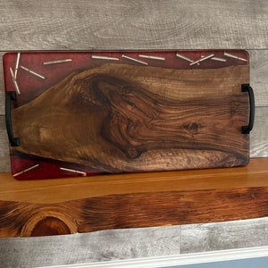 May include: A wooden serving tray with a red epoxy resin inlay and silver bullet casings. The tray has two black metal handles on the sides.