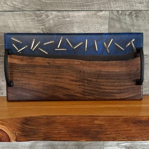 May include: A wooden serving tray with a blue epoxy resin inlay and bullet casings embedded in the resin. The tray has black metal handles.
