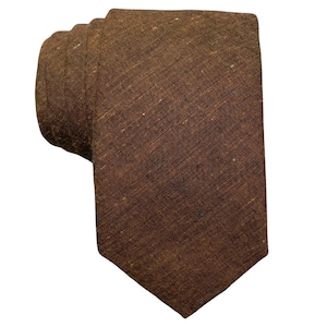 May include: A rolled-up brown tie with a textured appearance. The tie is a solid color, with subtle variations in tone and texture. The fabric appears to be a woven material.