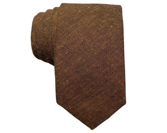 May include: A rolled-up brown tie with a textured appearance. The tie is a solid color, with subtle variations in tone and texture. The fabric appears to be a woven material.