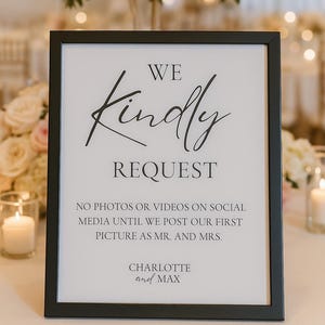 May include: A framed sign with the text "WE Kindly REQUEST" in elegant black script. The sign also requests no photos or videos on social media until the first picture is posted as Mr. and Mrs. The names Charlotte and Max are at the bottom.