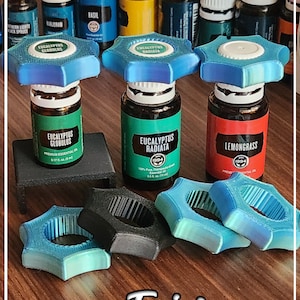 May include: Three blue star-shaped bottle stoppers with the text "Eucalyptus Globulus", "Eucalyptus Radiata", and "Lemongrass" on the bottles. The stoppers are on top of essential oil bottles. There are several other essential oil bottles in the background. The text "Twisturn" is on the wooden surface.