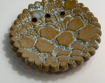 Może przedstawiać: Okrągłe mydelniczkę ceramiczne z falistym brzegiem i fakturowaną, jasnobrązową i niebieską glazurą.