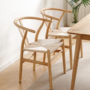 Könnte beinhalten: Zwei Holzstühle mit geflochtenen Rohrseats. Die Stühle haben eine gebogene Rückenlehne und einen Y-förmigen Rahmen. Die Stühle sind hellbraun und stehen auf einem hellbraunen Holzboden.