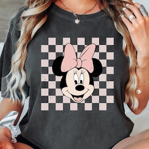 May include: A dark gray t-shirt with a pink and white checkered pattern and a cartoon image of Minnie Mouse with a pink bow.