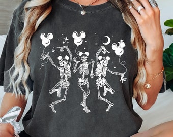 May include: A dark gray t-shirt with a graphic of three skeletons dancing with Mickey Mouse ears and holding balloons. The skeletons are wearing Mickey Mouse gloves. The text "Boo!" is printed on the shirt.
