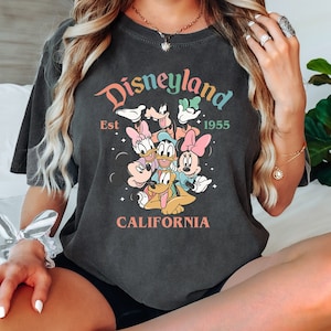May include: A dark gray t-shirt with a graphic print of Mickey Mouse and friends. The text "Disneyland Est 1955 California" is printed on the shirt.