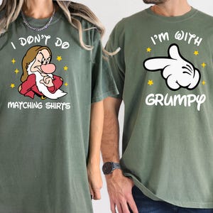 May include: Two green t-shirts with a matching design. One shirt features a cartoon image of Grumpy from Snow White and the text "I don't do matching shirts". The other shirt features a white cartoon hand pointing to the right with the text "I'm with Grumpy".