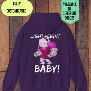 Puede incluir: Sudadera con capucha morada con un gráfico de un personaje Hello Kitty musculoso con el texto "LIGHTWEIGHT BABY!" impreso en la espalda.