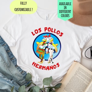 Peut inclure: T-shirt blanc avec un graphique de deux poulets de dessin animé portant des sombreros et le texte "Los Pollos Hermanos".