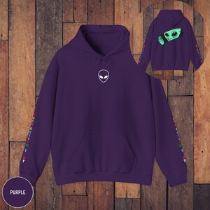 Peut inclure: Sweat-shirt &agrave; capuche violet avec un motif d'alien blanc sur le devant et du texte arc-en-ciel sur les manches. Le texte dit "YOUR CUSTOM TEXT".