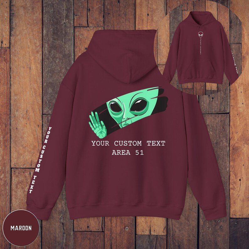 Peut inclure: Sweat-shirt &agrave; capuche bordeaux avec un extraterrestre vert qui sort d'un trait de peinture blanc. Le texte "YOUR CUSTOM TEXT AREA 51" est imprim&eacute; sur le sweat-shirt. Les mots "YOUR CUSTOM TEXT" sont imprim&eacute;s verticalement sur la manche.