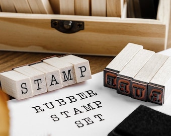May include: A wooden rubber stamp set with individual letter blocks spelling "STAMP" and "RUBBER STAMP SET". The set includes a wooden storage box and a black ink pad. The letters are in a classic serif font.