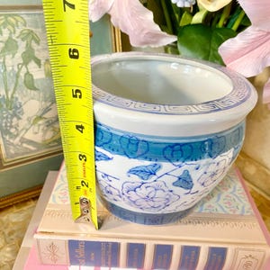 May include: A blue and white ceramic planter with a floral design. The planter is approximately 5 inches tall and is sitting on a stack of books.