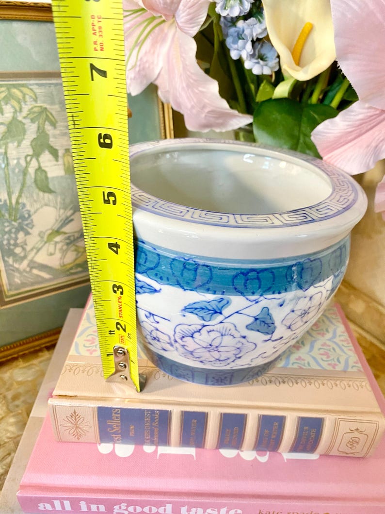 May include: A blue and white ceramic planter with a floral design. The planter is approximately 5 inches tall and is sitting on a stack of books.