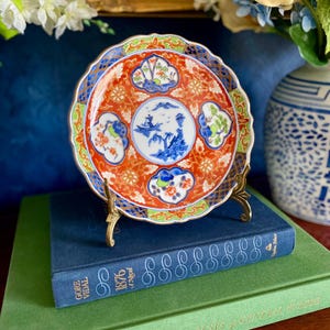 May include: A white ceramic mug with a black handle and the text "But First, Coffee" in a bold, black font. The mug is set against a blurred background, suggesting a cozy setting.