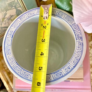 May include: A white ceramic planter with a blue and white geometric pattern around the rim. The planter is 6 inches in diameter.