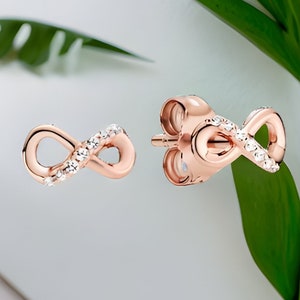 May include: A pair of rose gold infinity earrings with small clear cubic zirconia stones.