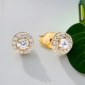 May include: A pair of gold stud earrings with a round halo of small diamonds surrounding a larger centre diamond.