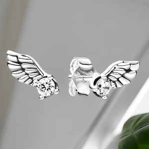 Può includere: Un paio di orecchini d'argento con un design ad ala e un cristallo trasparente al centro di ogni ala.