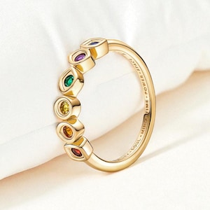 May include: A gold-colored ring with seven colorful gemstones. The gemstones are oval-shaped and arranged in a row. The ring has the words "SOUL - MIND - TIME - POWER - SPACE" engraved on the band.
