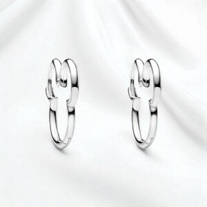 Pu&ograve; includere: Un paio di orecchini a cerchio color argento. Ogni orecchino presenta un design unico con due anelli ad incastro, creando un look moderno ed elegante. Gli orecchini sono esposti su uno sfondo bianco.