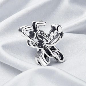 May include: A silver-colored ring with an intricate, openwork design. The ring features a complex pattern of curved lines and shapes, creating a unique and artistic appearance. The ring is displayed on a white, silky fabric.