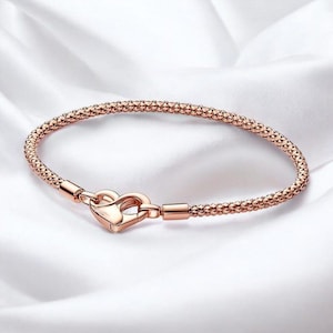 以下が含まれることがあります： ローズゴールドのブレスレット。テクスチャード加工されたビーズのデザイン。ブレスレットはハート型の留め金が付いています。ジュエリーは白くシルキーな背景に展示されています。