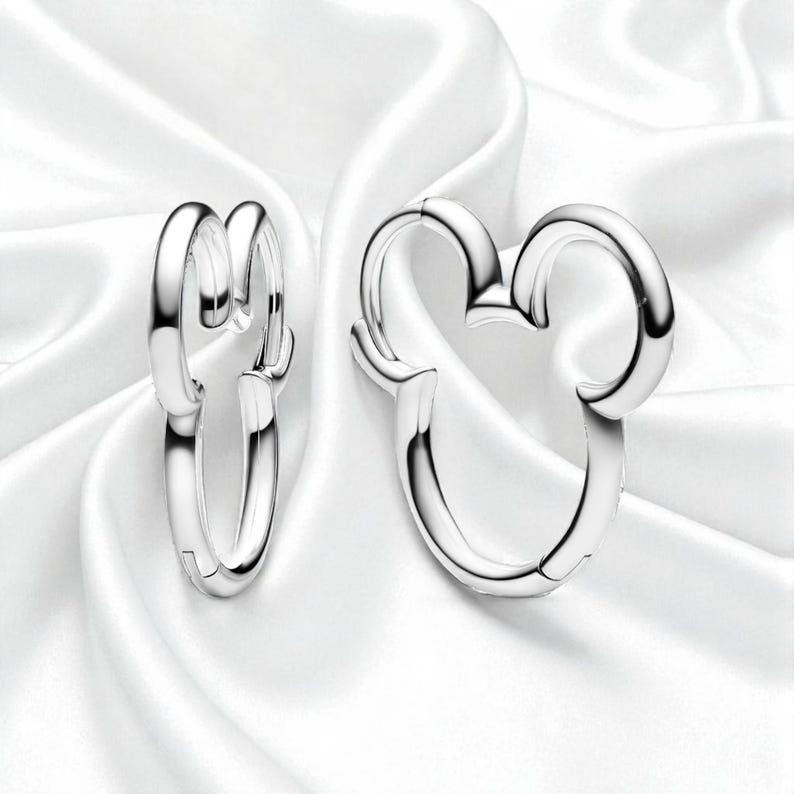 Pu&ograve; includere: Un paio di orecchini a cerchio color argento. Uno &egrave; a forma di testa di topo classica, l'altro &egrave; un semplice cerchio. Gli orecchini sono presentati su uno sfondo bianco e setoso.