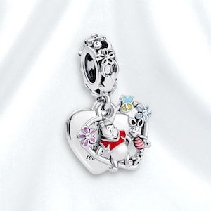 Puede incluir: Un charm de plata con Winnie the Pooh y Piglet dentro de un colgante en forma de corazón. El charm incluye acentos florales coloridos y las palabras "We" y "Forever". El charm está diseñado para ser adjuntado a una pulsera o collar.