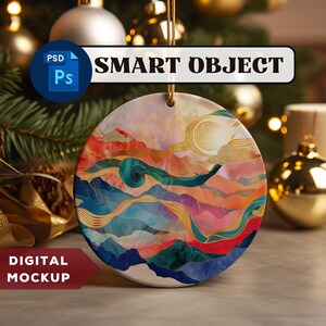Op de afbeelding: Een ronde keramische kerstbal met een kleurrijk abstract ontwerp met een zonsondergang boven bergen en een halve maan. De kerstbal is versierd met gouden accenten en heeft een witte achtergrond.