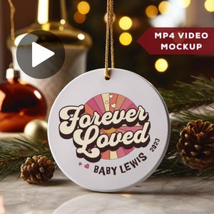 May include: White ceramic Christmas ornament with a pink and orange sunburst design and the text "Forever Loved" in a retro font. The ornament also includes the text "Baby Lewis 2023".