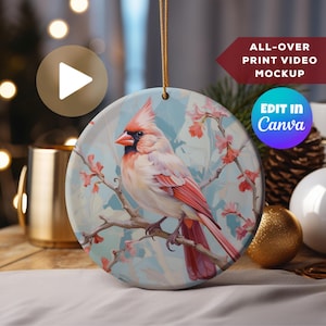 May include: A round ceramic ornament featuring a detailed painting of a cardinal bird perched on a branch with pink blossoms. The ornament has a blue and white background and is perfect for adding a touch of nature to your holiday decor.