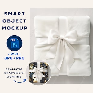 May include: A white gift box with a white satin ribbon and bow. The box is sitting on a light gray surface. The box is decorated with a black and gold patterned gift wrap.