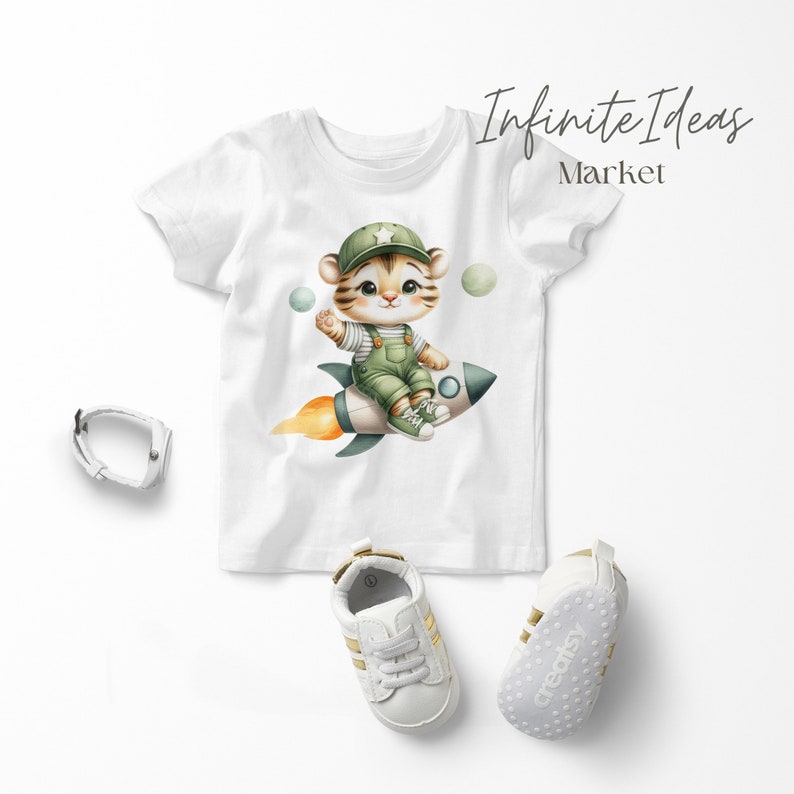 May include: White t-shirt with a cartoon tiger wearing a green hat and overalls, riding a rocket with flames. The tiger is holding a star. There are three green and white planets in the background. The text "Infinite Ideas Market" is in the top right corner.