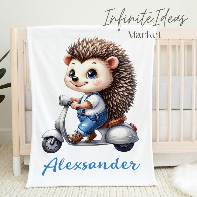 May include: White baby blanket with a cartoon hedgehog riding a scooter. The hedgehog is wearing blue overalls and has brown eyes. The blanket has the name "Alexander" printed in blue letters.