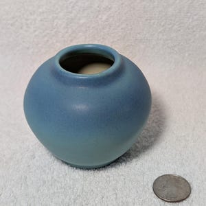 May include: A small, round, blue ceramic vase with a light blue glaze. The vase is about 3 inches tall and has a slightly rounded rim.