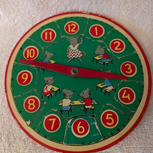 May include: A vintage wooden toy clock with a green face and red numbers. The clock features a red pointer and a scene of mice in a classroom. The clock is in good condition with some wear and tear.