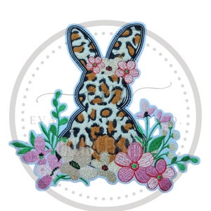 May include: Embroidered patch of a leopard print bunny wearing a flower crown. The bunny is surrounded by green leaves and pink flowers.