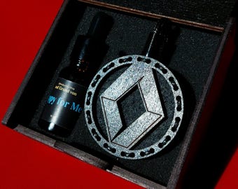 Könnte beinhalten: Eine schwarze Holzkiste mit einem silbernen und schwarzen geometrischen Design-Anhänger und einer kleinen Flasche mit einem schwarzen Etikett, auf dem "Grand von" und "Happy for Me" steht.
