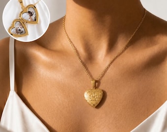 May include: A gold-toned heart-shaped locket necklace featuring an engraved paw print on the front. The locket is suspended from a delicate gold chain. An inset shows the locket open, revealing two small photographs of a dog inside the heart-shaped frame.