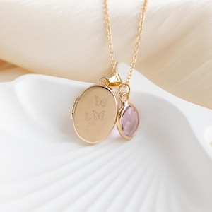 May include: Gold chain necklace with a locket pendant featuring an engraved butterfly design and a small, oval-shaped, light purple gemstone charm.