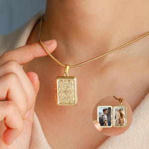 Può includere: Un ciondolo a medaglione rettangolare color oro su una catena a serpente abbinata. Il medaglione presenta un intricato motivo floreale in rilievo sul davanti. Una volta aperto, il medaglione rivela due cornici interne con piccole foto di due persone.