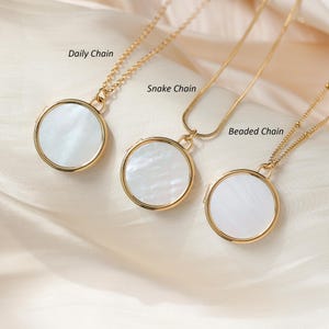 May include: Three gold necklaces with different chain styles: daily chain, snake chain, and beaded chain. Each necklace features a round white mother-of-pearl locket.