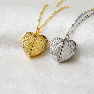 May include: Two heart-shaped lockets on delicate chains, one in a polished gold tone and one in a polished silver tone. Each locket features a detailed embossed wing design on the front surface, creating a textured appearance across the heart.