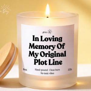 May include: A lit, frosted glass candle with a wooden lid. The candle has a white label with the text "In Loving Memory Of My Original Plot Line." It is hand-poured and has a clean burn, with no toxic vibes.