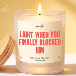 May include: A lit, frosted glass candle with a wooden lid. The candle has a label with the text "LIGHT WHEN YOU FINALLY BLOCKED HIM" in red. The candle is 7 oz and has a 35-hour burn time.