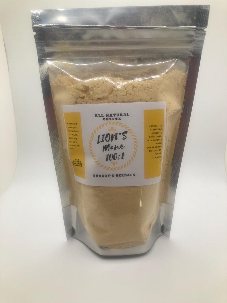 May include: A clear, resealable pouch filled with light brown powder. The pouch has a silver metallic top. A yellow label reads "Lion's Mane 100:1" and "Shaggy's Herbals". The label also states "All Natural Organic".
